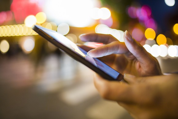 Person's hands holding a smartphone, city lights in the background.