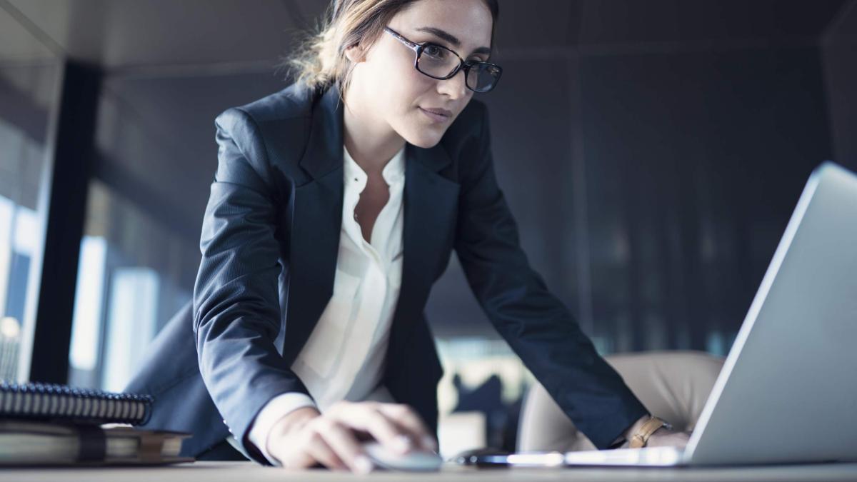 A woman leaning over a table to use a laptop