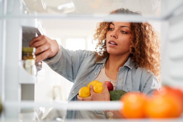 A woman putting fruits and vegetables away in her refrigerator.