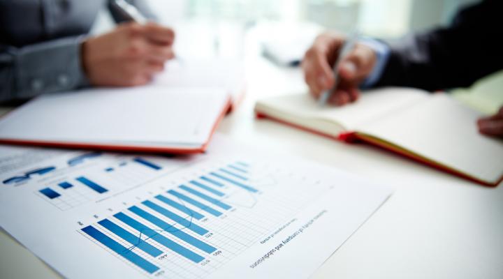 Generic image of two people with notebooks surrounding a paper with charts on it