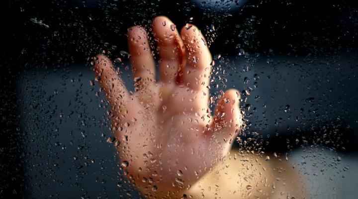 Hand pressed up against a rain-covered window