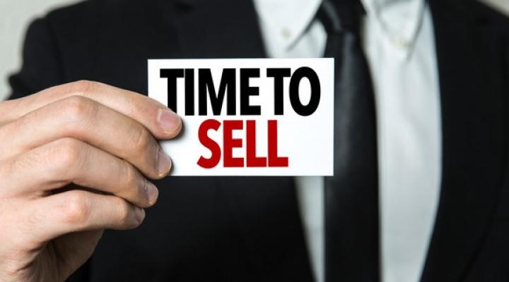 Man in business suit holds sign that says Time to Sell. 