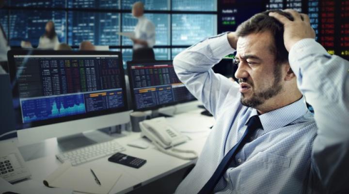 A frustrated investor clasping his head as he looks at losses on his computer screen.