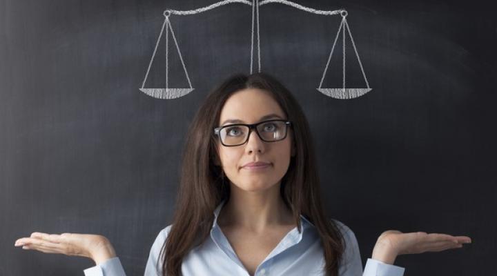 Woman in front of a chalkboard with an evenly balanced scale drawn behind her.