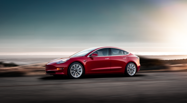 A red Model 3 driving at sunset