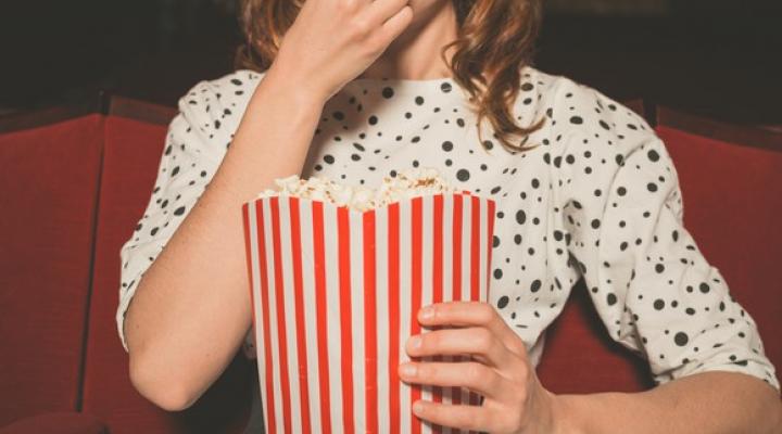 Picture of a woman sitting in a movie theater eating popcorn.