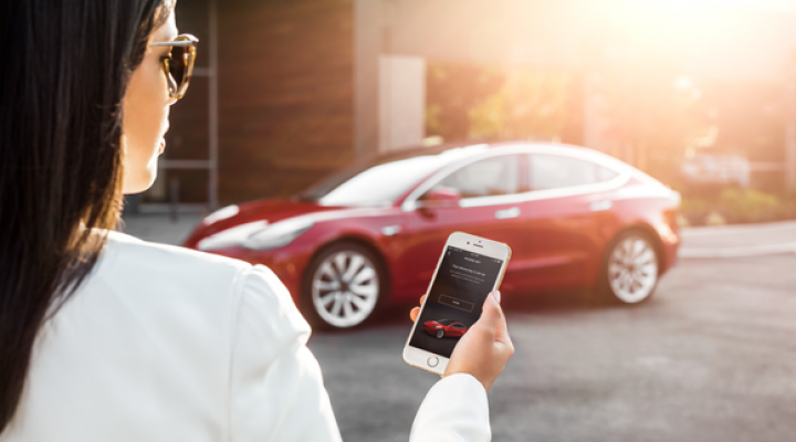 A woman unlocks her Model 3 with a Tesla app on her smartphone