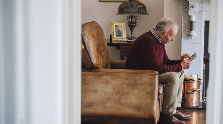 Senior man sitting in an armchair and holding a tablet.