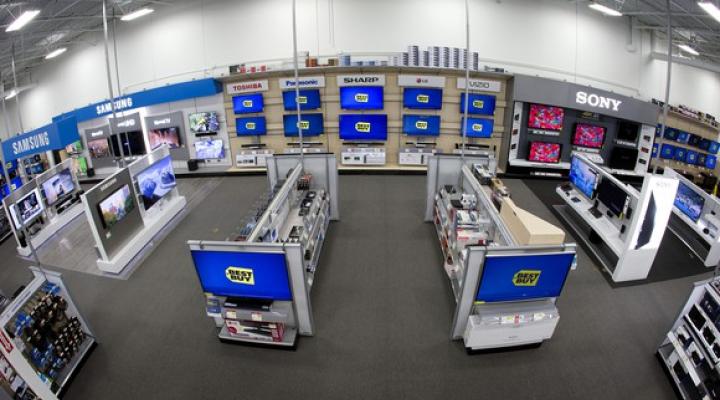 A view of a Best Buy home theater department, with TVs displayed on the wall and on two end caps.