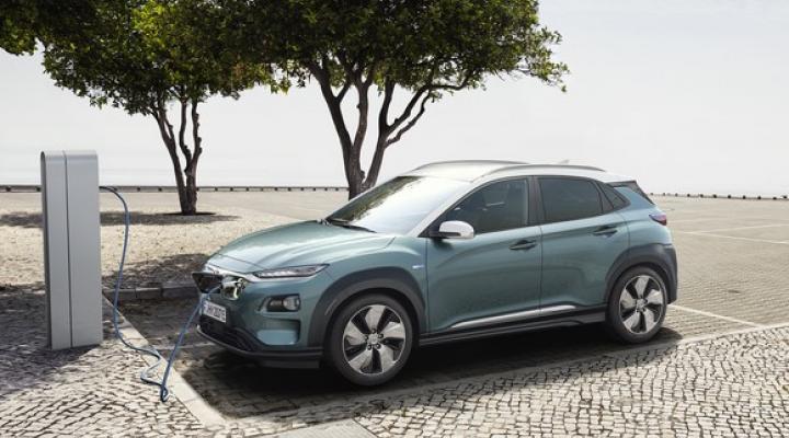 The new Hyundai Kona Electric, a small green crossover SUV, parked next to a charging station. 