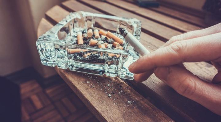 A hand holding a lit cigarette and ashing it into an ashtray.