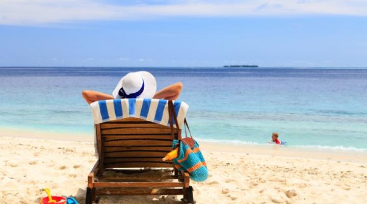 A woman sitting in a chair on a white sand beach looking out at the ocean.