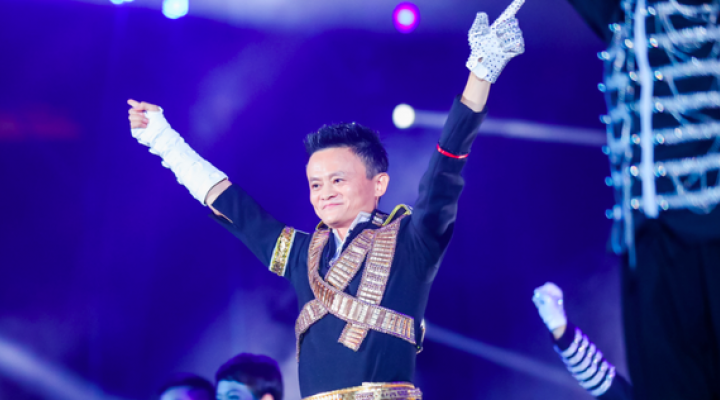 Alibaba cofounder Jack Ma lifts his arms up in victory while speaking on stage at an event.