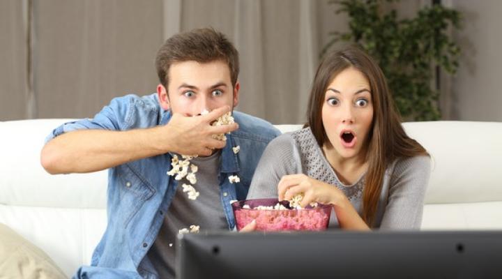 A young couple shoveling popcorn into their mouths, staring wide-eyed at the TV screen.