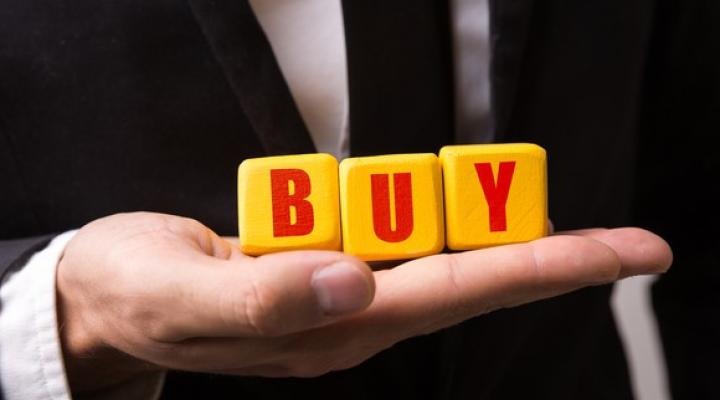 Yellow blocks spelling out Buy in red letters on a man's hand.