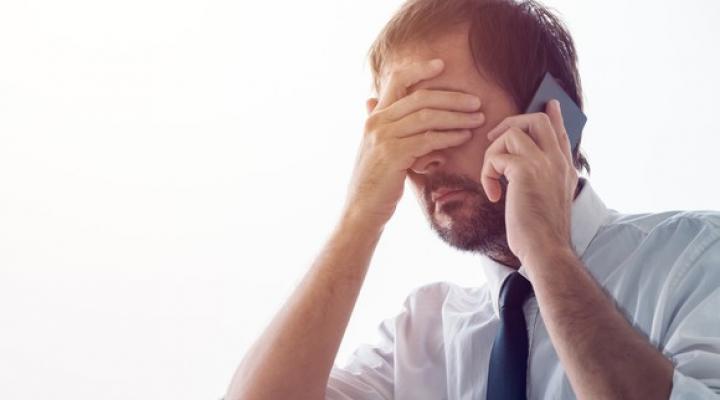 A person in a suit with their hand over their face talking on phone.