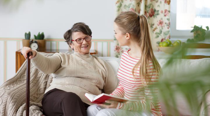 An older parent sits on a sofa with a teenager.