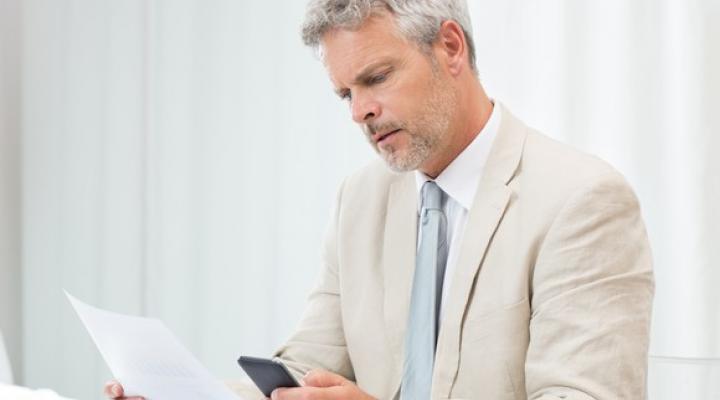 Senior man in a suit looking at a phone and a document