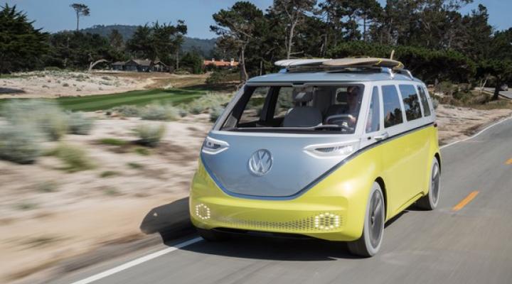 The VW I.D. Buzz concept, an electric minivan with styling that recalls VW's iconic 1960s Mircrobus, is shown driving on a beach road in California, with two surfboards on its roof rack.