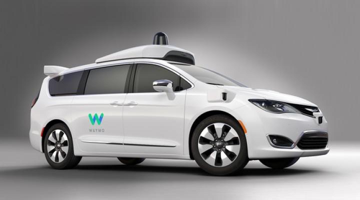 A white Chrysler Pacifica Hybrid minivan with Waymo's logo and self-driving sensor hardware.