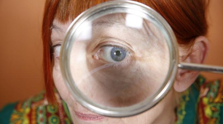 A retiree looking through a large magnifying glass.