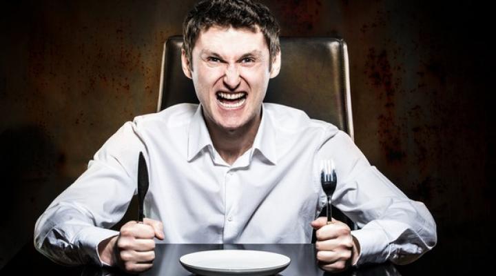 Angry man holds knife and fork in front of empty plate