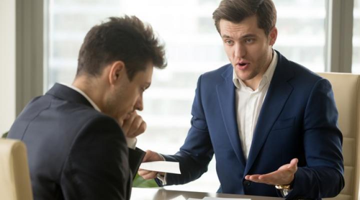 Man in suit looking critically at a second professional male who's looking down.