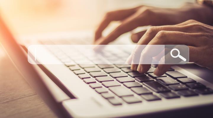 Hands typing on the keyboard of a laptop computer with the overlay of a search box in the center.