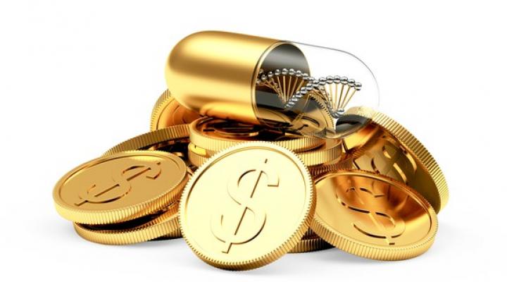 A gold pill sits atop a pile of gold coins.