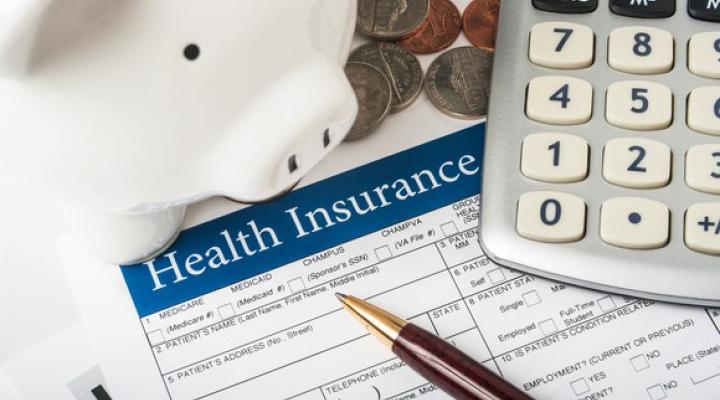 Health insurance form with pen, calculator, piggy bank, and coins