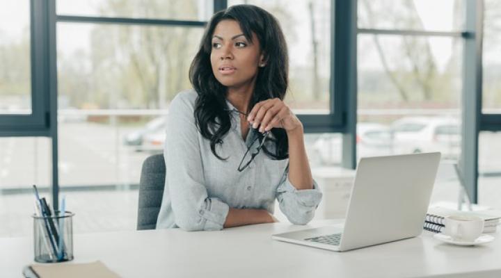 Businesswoman sits at a desk looking pensive.