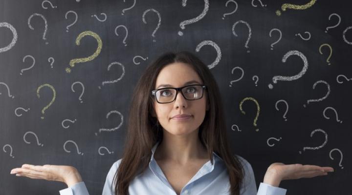 A woman in front of a blackboard with question marks written on it.